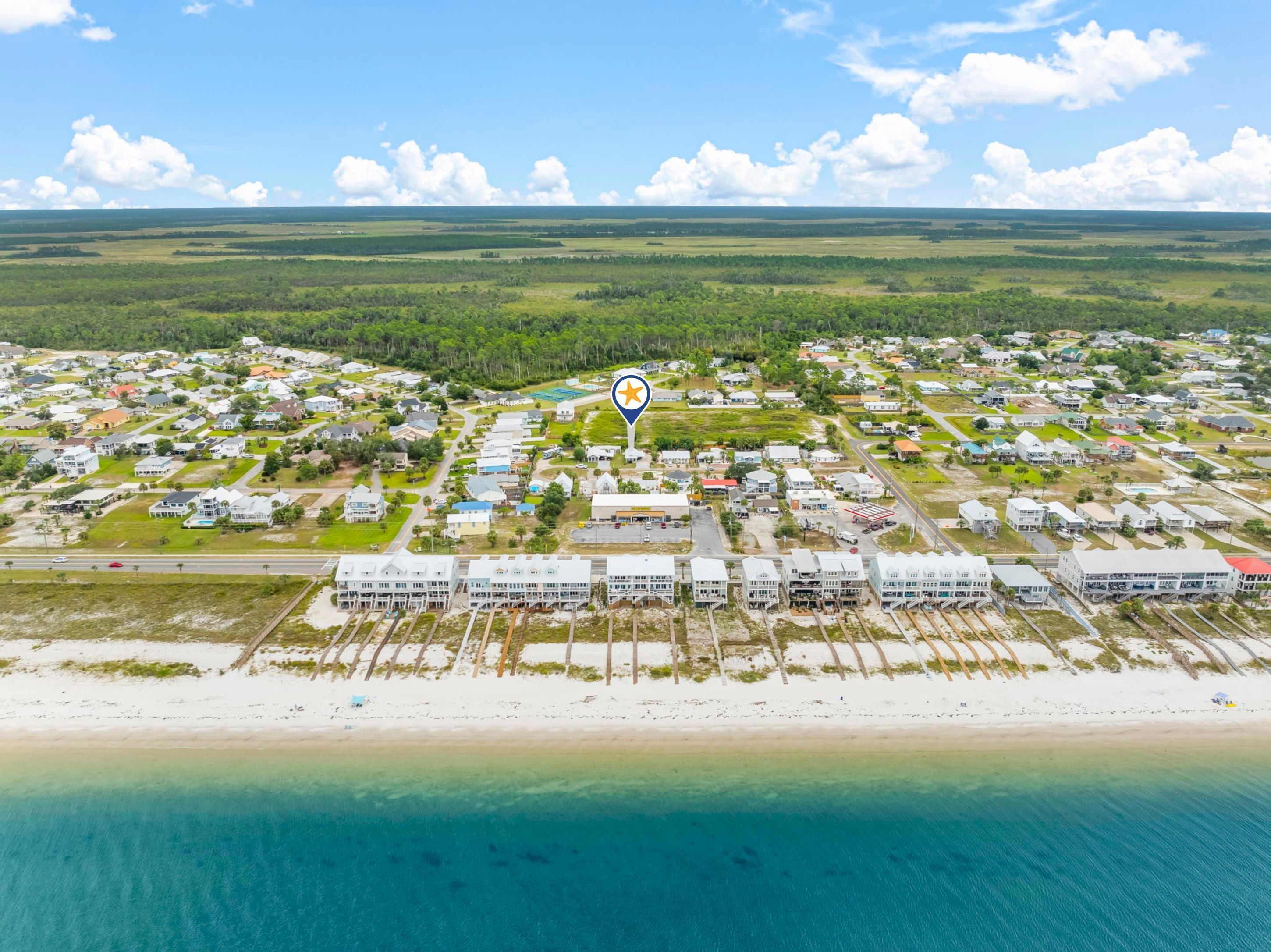 Luchtbeeld van een kustgebied met huizen, een strand en een aangegeven locatie.