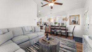 A modern living room with a gray sofa, a wooden coffee table, and a ceiling fan. - Beach House - Sun-kissed Cottage by PHG (Port St. Joe)