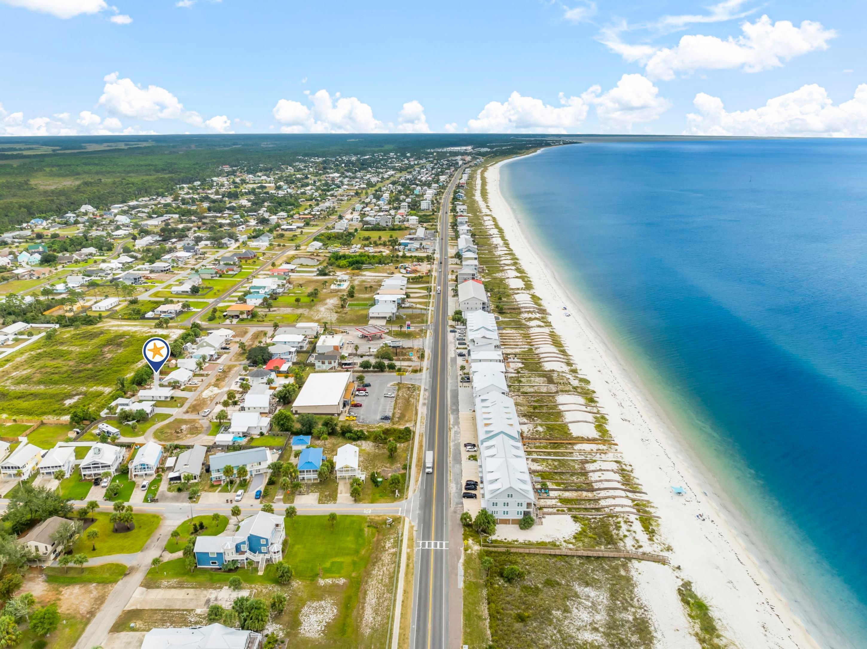 An aerial view of a coastal town with a long beachfront, roads, and residential areas.
