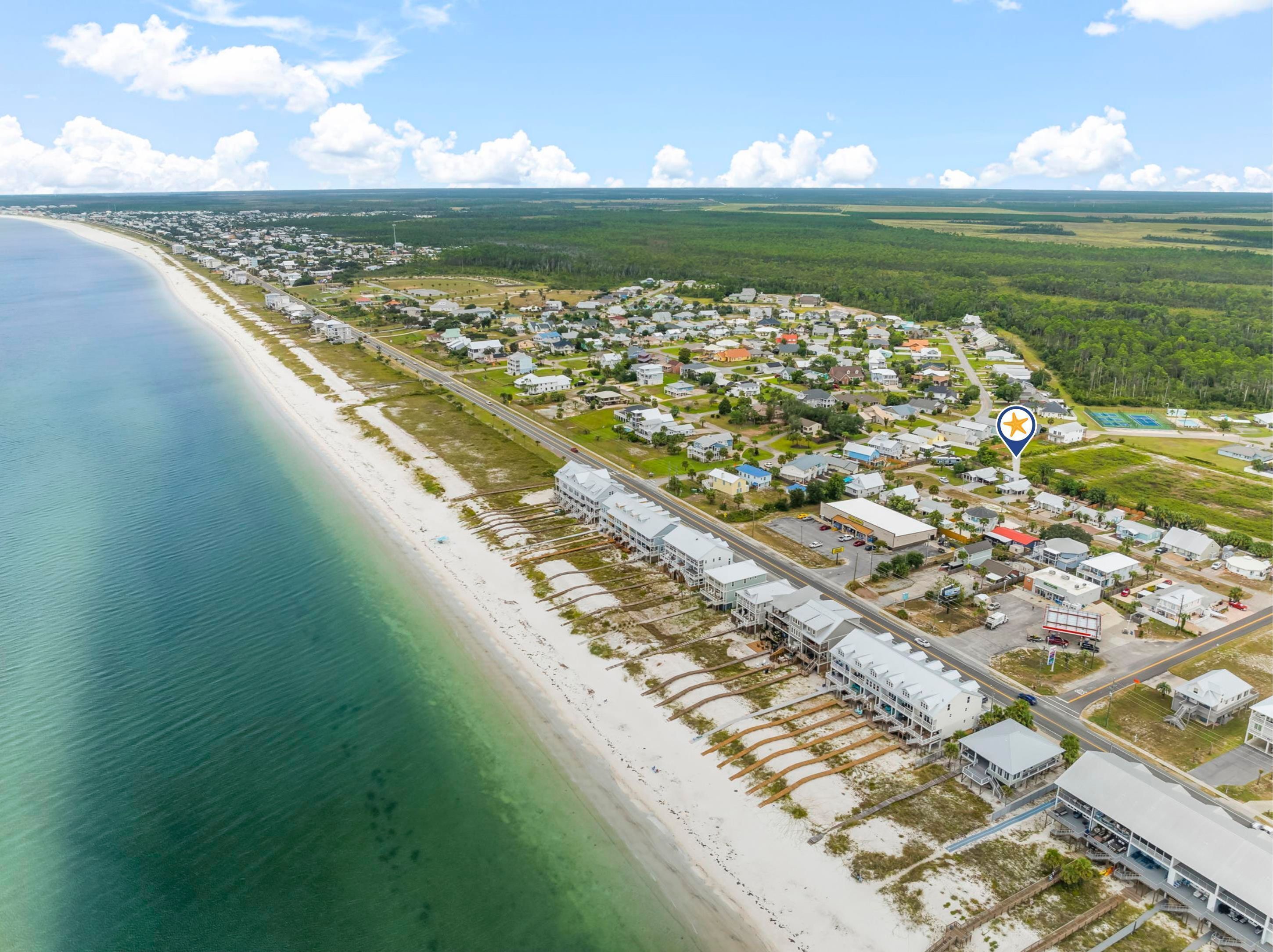An aerial view of a coastal town with a beach, residential areas, and a prominent hotel with a large building and multiple stories.