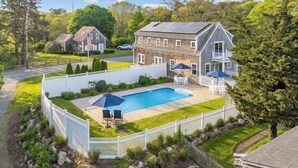 Une grande maison avec une piscine, entourée d’une clôture blanche, et un drapeau devant.