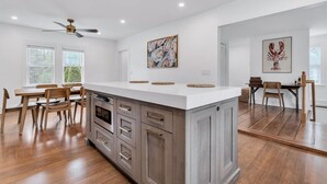 Une cuisine moderne avec des meubles en bois, un plan de travail blanc et un coin repas doté de chaises en bois.