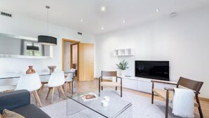 A modern living room with a glass coffee table, a sofa, a TV, and a dining area with chairs and a table.