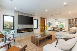 A modern living room with a fireplace, a flat-screen TV, and a dining area with a table and chairs.