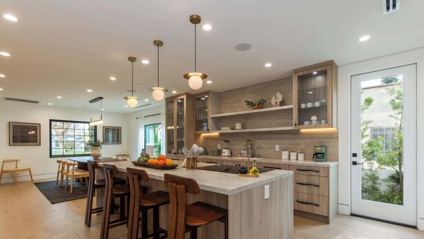 Una cocina moderna con una isla central, taburetes de madera, iluminación colgante y vistas a zonas verdes.