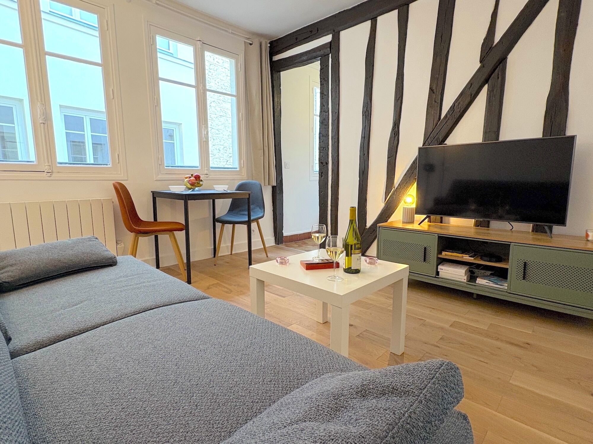 A modern living room with a large flat-screen TV, a sofa, a dining table with chairs, and a small cabinet.