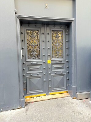 A gray double door with ornate metalwork and a yellow doormat. - Le studio Saint Merri (Paris)