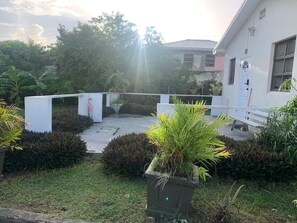 A courtyard with a white building, potted plants, and a pathway leading to a door. - Tonia’s place, Entire condo in Bridgetown, Barbados (Bridgetown)