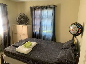 A single bed with a patterned bedspread, a fan, curtains, and a birthday balloon. - Tonia’s place, Entire condo in Bridgetown, Barbados (Bridgetown)
