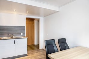 Une cuisine moderne avec des meubles blancs, une porte en bois et un coin repas comprenant deux chaises noires et une table en bois.