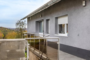 Un bâtiment à l’extérieur gris, une fenêtre avec un store blanc et une rambarde en métal.