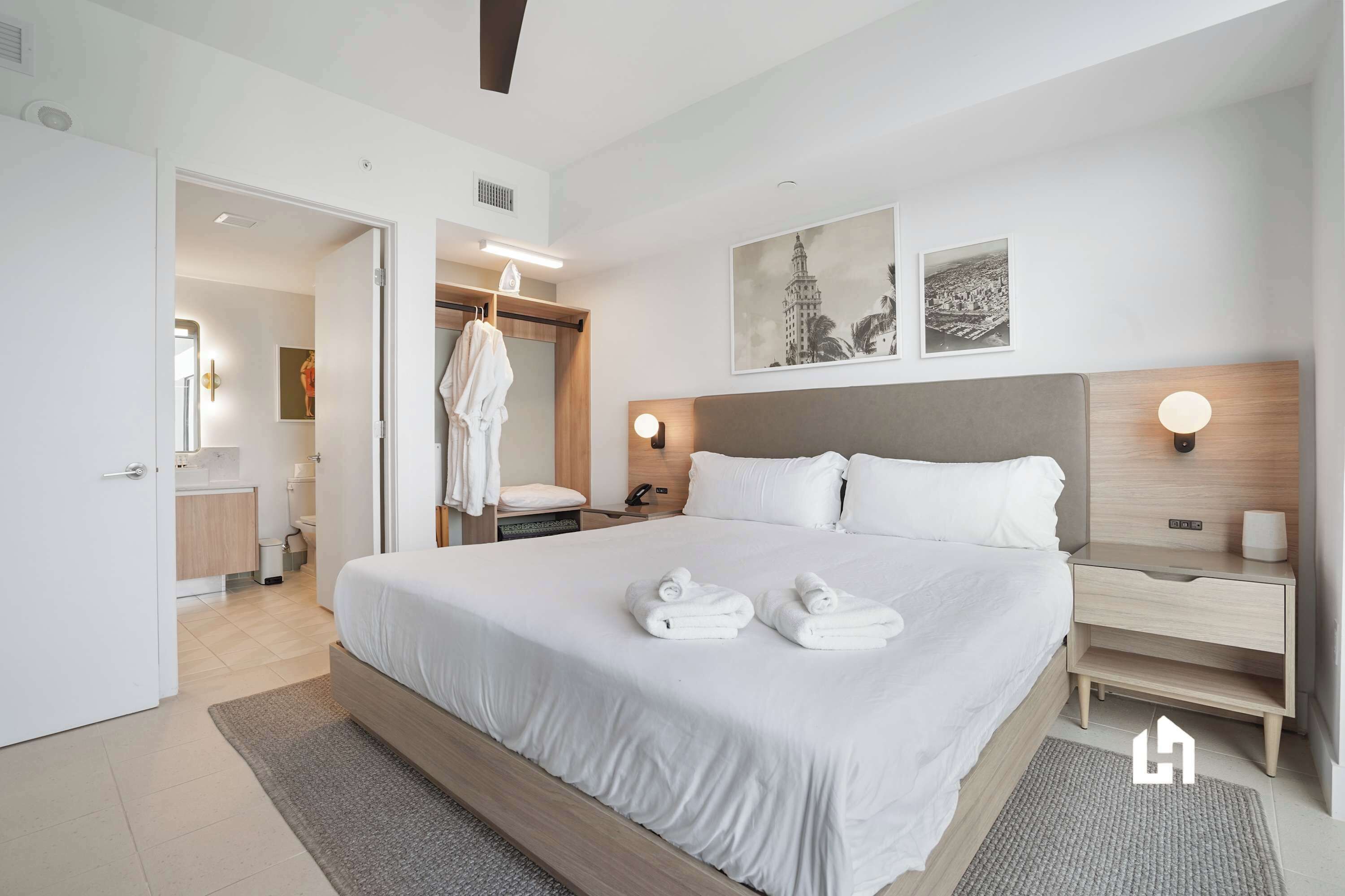 Una habitación de hotel moderna con una cama grande, mesitas de noche, un armario y obras de arte en las paredes.
