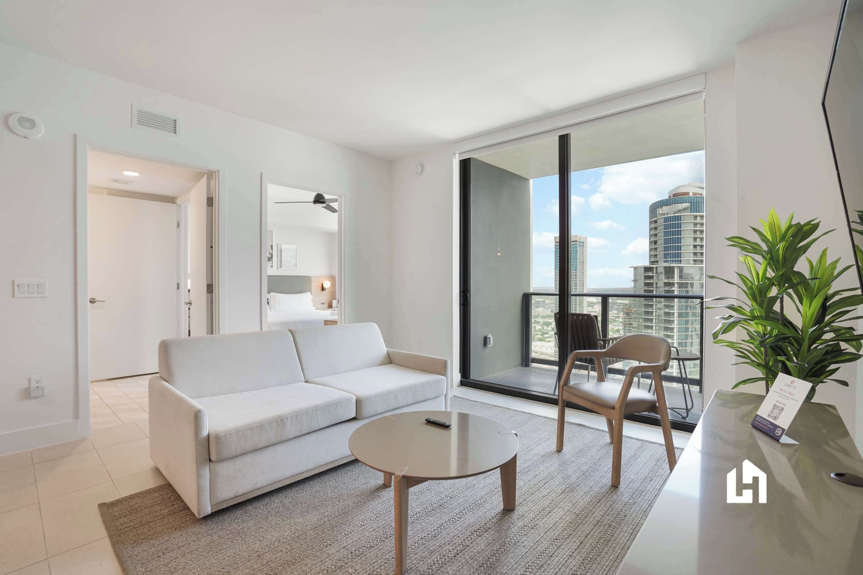A modern living room with a sofa, a coffee table, and a balcony with a view of the city.