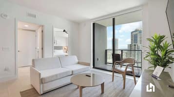 A modern living room with a sofa, a coffee table, and a balcony with a view of the city.