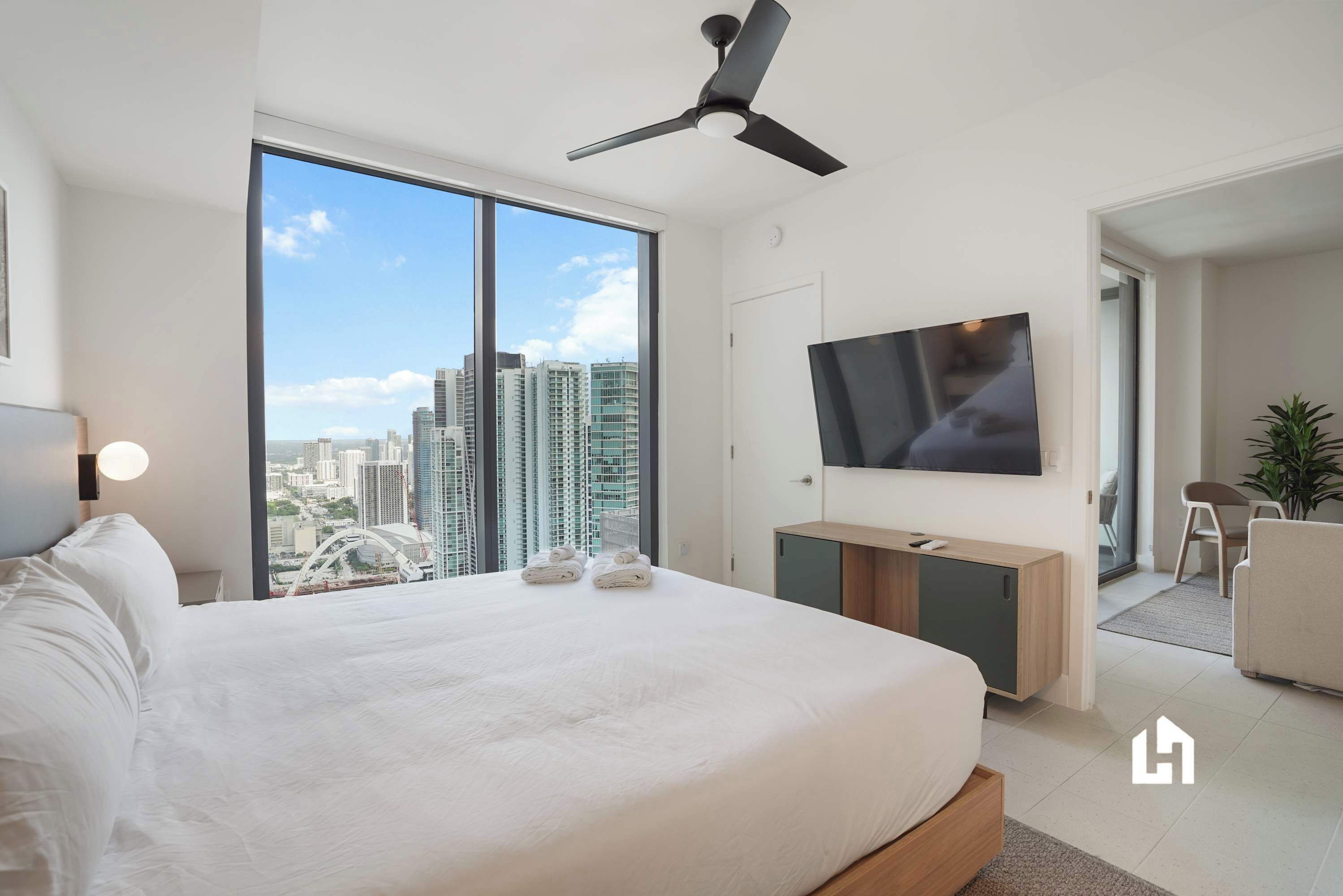 A modern hotel room with a large bed, a ceiling fan, a TV, and a city view.