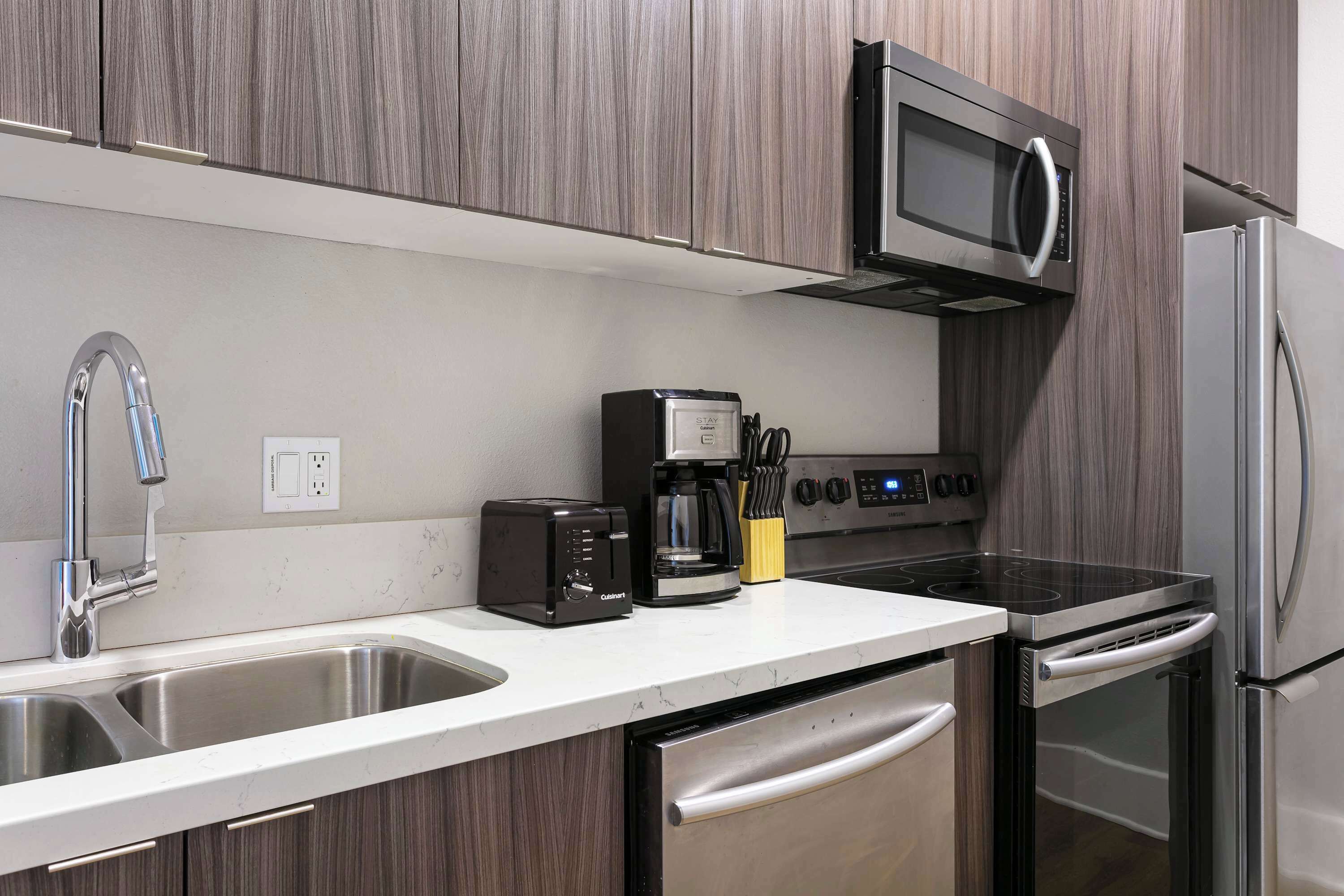 A modern kitchen with a stainless steel sink, a built-in microwave, a coffee maker, a toaster, and an oven.