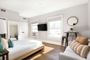 Quarto moderno com cama, sofá, mesinha e TV fixada na parede.