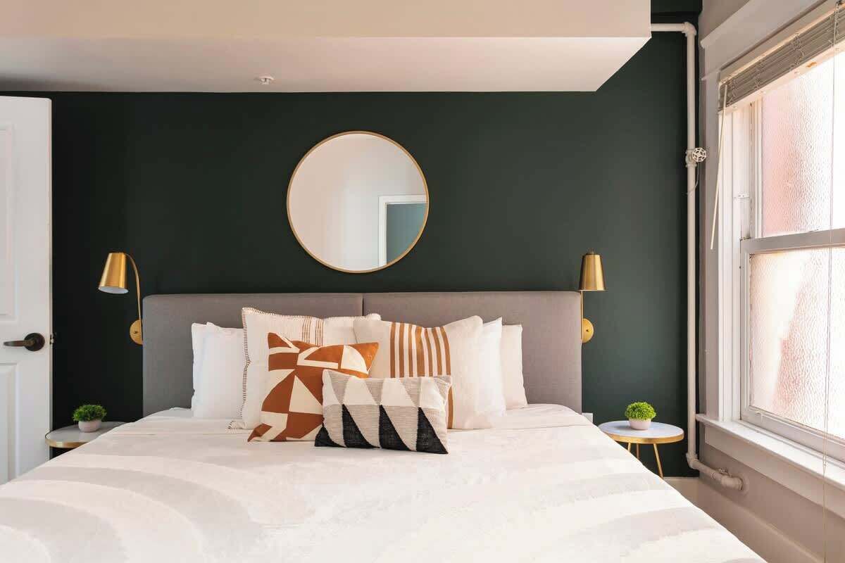 Une chambre à coucher avec un lit, un miroir rond, deux lampes de chevet et une fenêtre avec des stores.