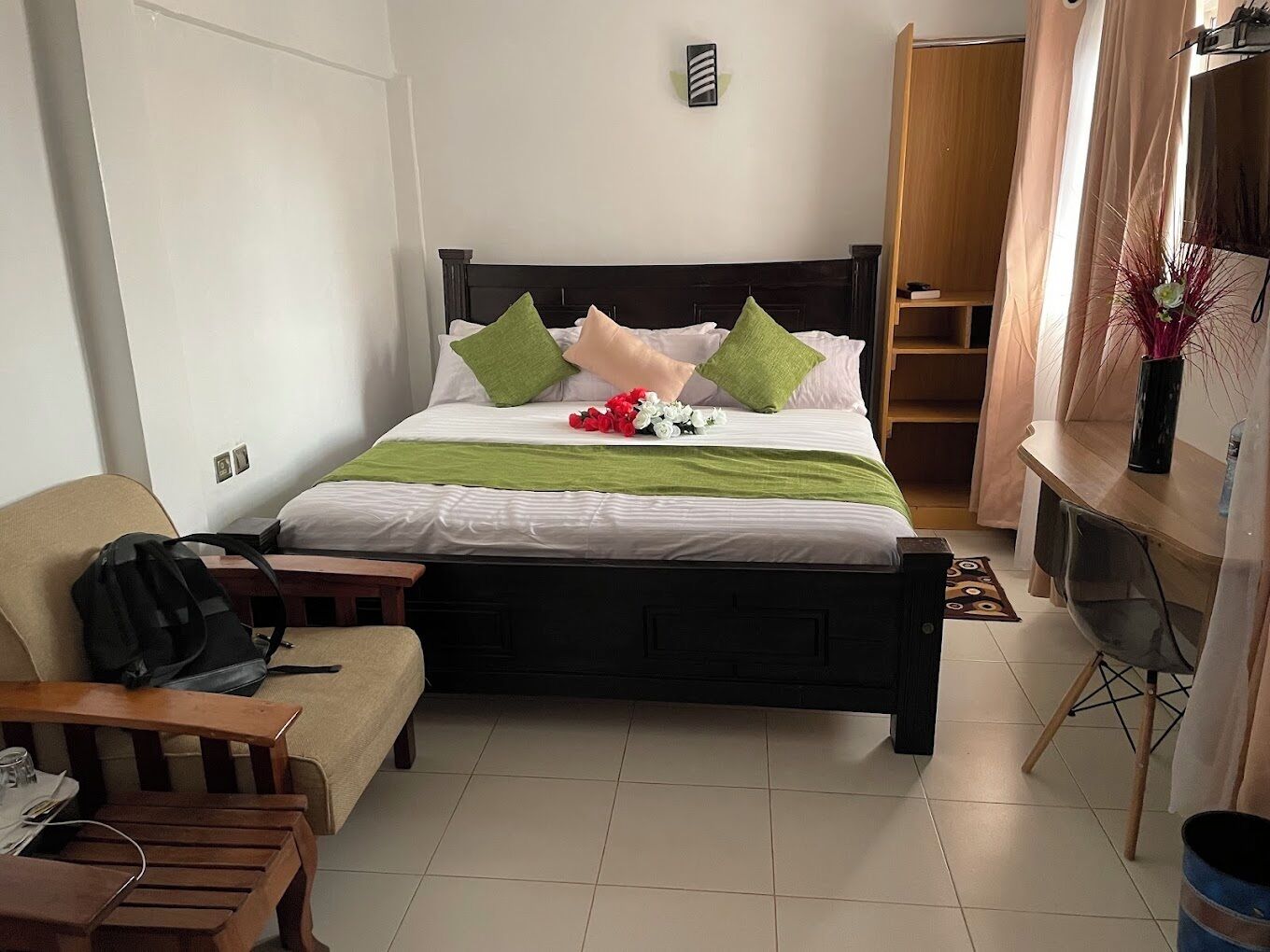 A neatly arranged hotel room with a bed, a wooden bench, a small table with a chair, and a wardrobe.