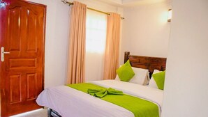 Een hotelkamer met een houten deur, een bed met wit beddengoed en groene accenten, en beige gordijnen.