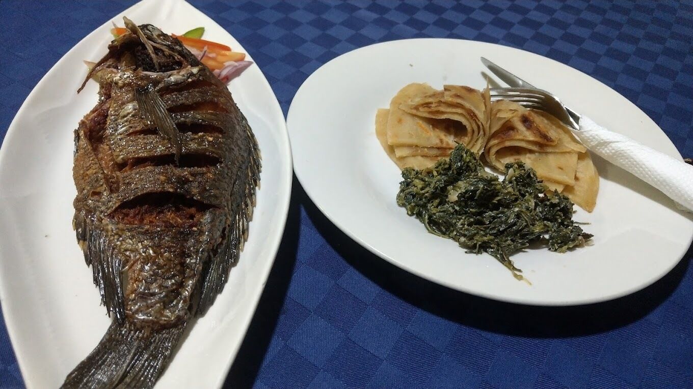 A plate with a whole fish and a plate with flatbreads and greens.