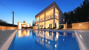 Een modern huis met twee verdiepingen en een zwembad op de voorgrond.