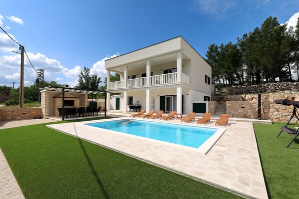Una casa a due piani con piscina, area relax esterna e un muro in pietra.