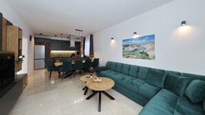 Een moderne woonkamer met een groene bank, een houten salontafel en een eethoek met stoelen en een tafel.