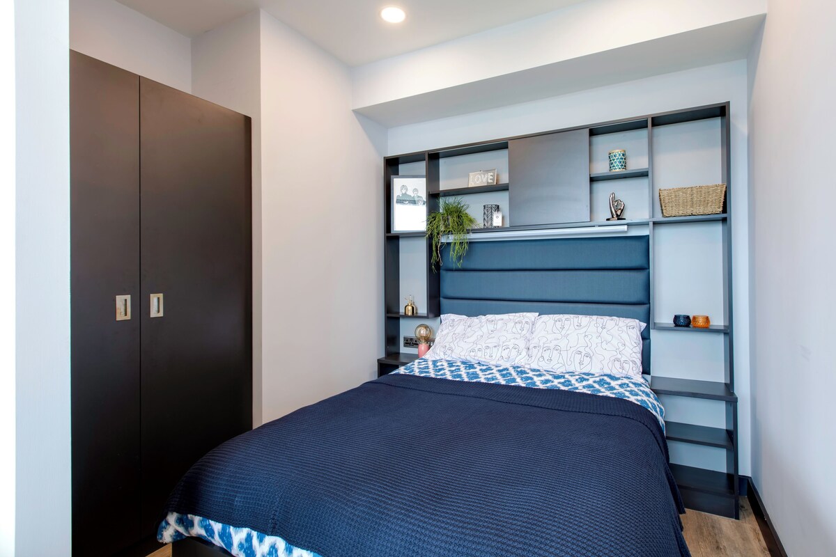 A bedroom with a bed, a wardrobe, and built-in shelving with decorative items.
