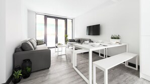 Ein modernes Wohnzimmer mit einem grauen Sofa, einem weißen Esstisch und einem flachbildfernseher an der Wand.