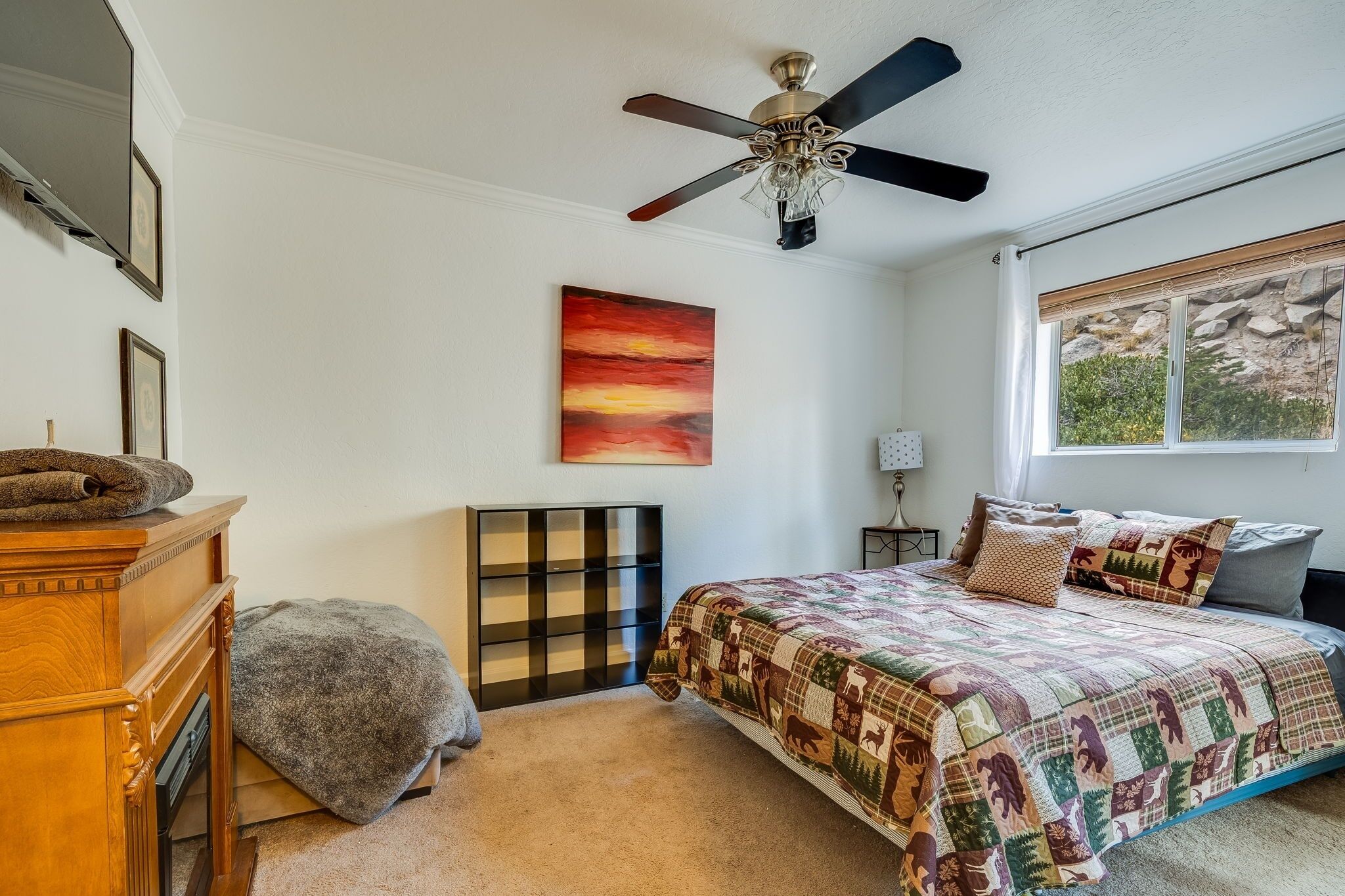 Une chambre à coucher comprenant un lit, un ventilateur de plafond, un tableau, une fenêtre avec vue et une commode.