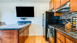 Une cuisine moderne avec des meubles en bois, un réfrigérateur noir, une cuisinière et un téléviseur à écran plat fixé au mur.