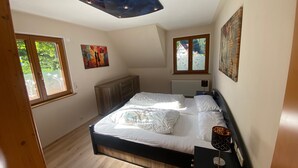 A bedroom with a bed, a wooden headboard, a ceiling light fixture, and two windows. - Apartment Sonnenblick with Mountain Views, Shared Garden and Wi-Fi (Bad Rippoldsau-Schapbach)