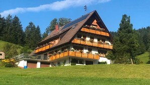 A multi-story chalet with a sloped roof, balconies with flower boxes, and a solar panel on the roof. - Apartment Sonnenblick with Mountain Views, Shared Garden and Wi-Fi (Bad Rippoldsau-Schapbach)