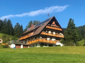 A multi-story chalet with a sloped roof, balconies with flower boxes, and a solar panel on the roof.