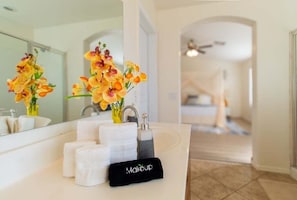 A bathroom with a white sink, a mirror, and a vase of flowers. There are towels and a makeup bag on the sink. - Casa Desert Willow - Stayshores 5 Bedroom Home (Casa Grande)