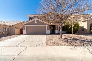 A residential house with a garage, a driveway, and a tree in the front yard. - Casa Desert Willow - Stayshores 5 Bedroom Home (Casa Grande)