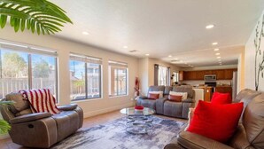 Un salon spacieux avec un canapé en cuir, un fauteuil inclinable et une table basse. De grandes fenêtres laissent entrer la lumière naturelle et offrent une vue sur l’extérieur.