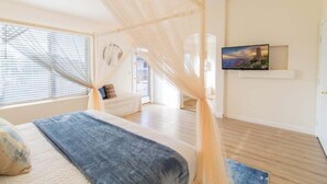 Une chambre à coucher avec un lit à baldaquin, un téléviseur fixé au mur et une vue sur l’extérieur par la fenêtre.