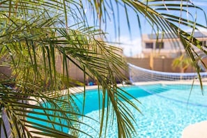 Una piscina con una hamaca y hojas de palmera al frente.