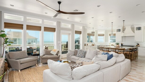 A spacious living room with a large white sofa, a coffee table, and a dining area with wooden chairs. - Casa Del Sol 4 Bedroom Home (Port Bolivar)