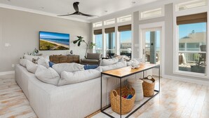 A spacious living room with a large sectional sofa, a wooden coffee table, and a ceiling fan. There is a large window providing a view of the outside. - Casa Del Sol 4 Bedroom Home (Port Bolivar)