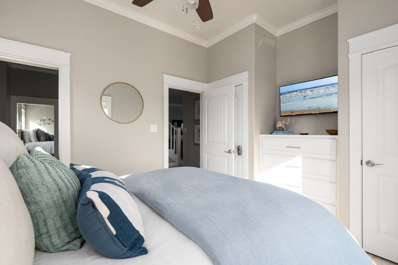 Un dormitorio con una cama, un televisor en la pared y una puerta que da a un pasillo.