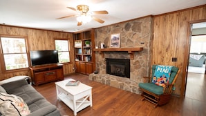 A living room with a stone fireplace, wooden walls, a television, and a rocking chair. - 371 Mountain Hill Rd, Fortson (Harris County)