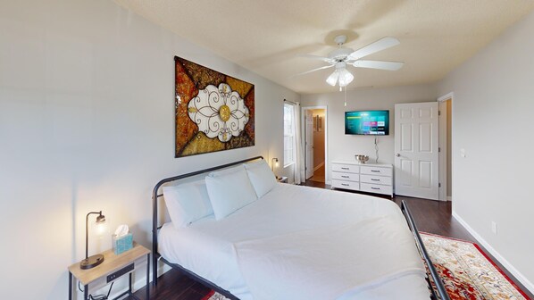 A bedroom with a bed, bedside table, lamp, artwork, ceiling fan, TV, dresser, and a door leading to another room. - 106 Middlebrook Dr, Cartersville (Cartersville)