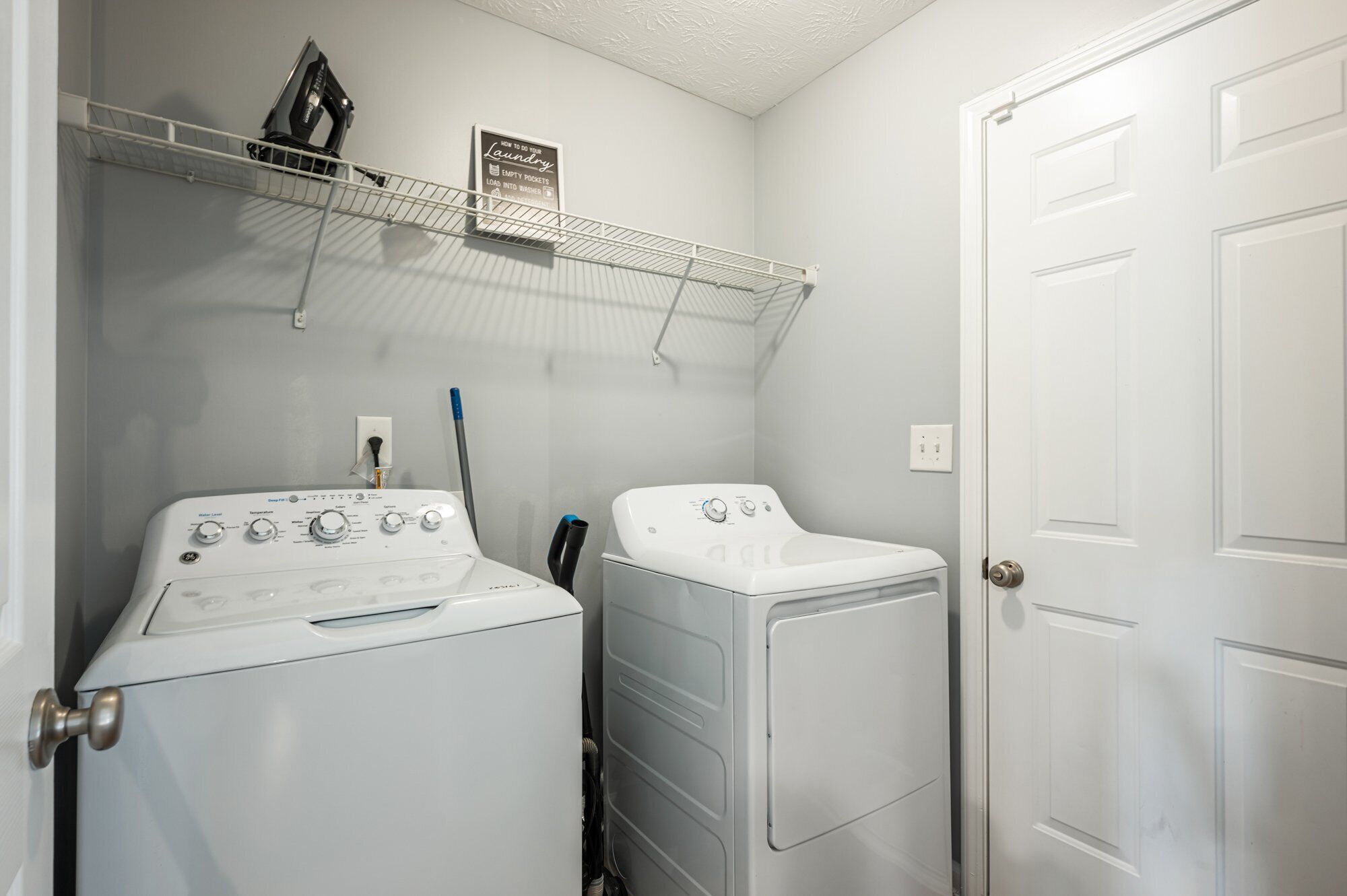 A laundry room with two white washing machines and a drying rack.