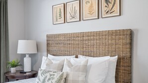 A bed with white bedding, a wicker headboard, and a nightstand with a lamp and a plant.