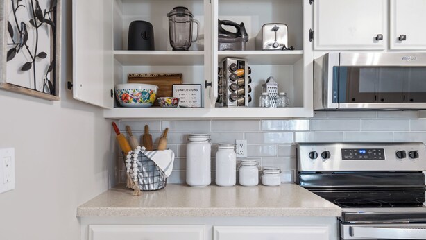 A kitchen with white cabinets, a microwave, an oven, and various kitchen utensils and appliances.