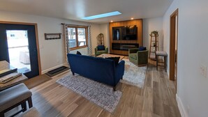 A modern living room with a blue sofa, green armchairs, a flat-screen TV, and a skylight.