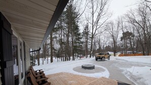 A wooden deck with a bench, a paved area with a circular feature, and a vehicle parked in a snowy landscape.